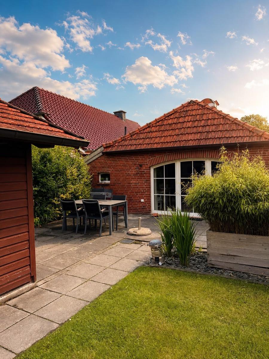 Roter Ziegeldach mit Terrasse, Grill und Gartenbereich unter blauem Himmel.