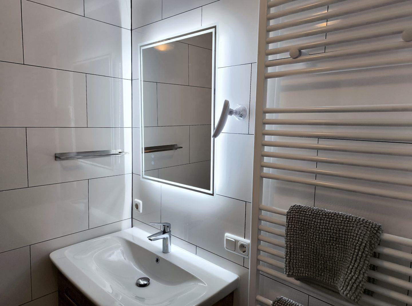 Badezimmer mit Waschbecken, beleuchtetem Spiegel und Heizkörper mit Handtuch.