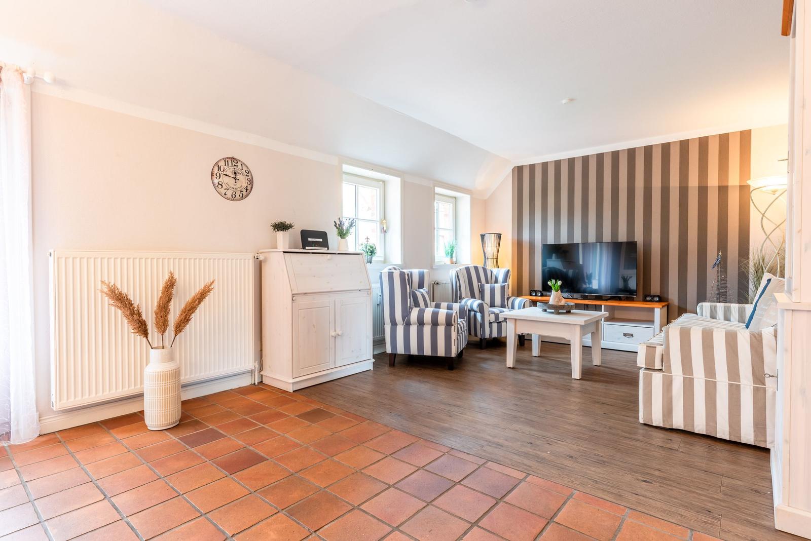 Wohnzimmer mit Sitzgruppe, Fernseher und Holzboden. Wand mit Streifenmuster. Terrakottafußboden im Vordergrund.