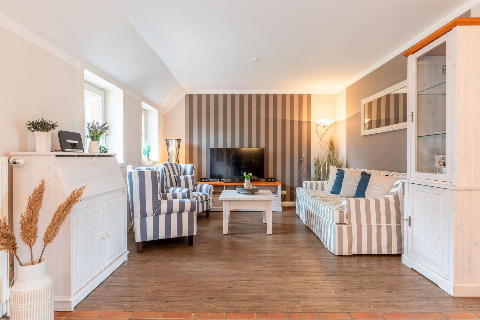 Wohnzimmer mit Sofa, Sessel, Fernseher und Holzboden.