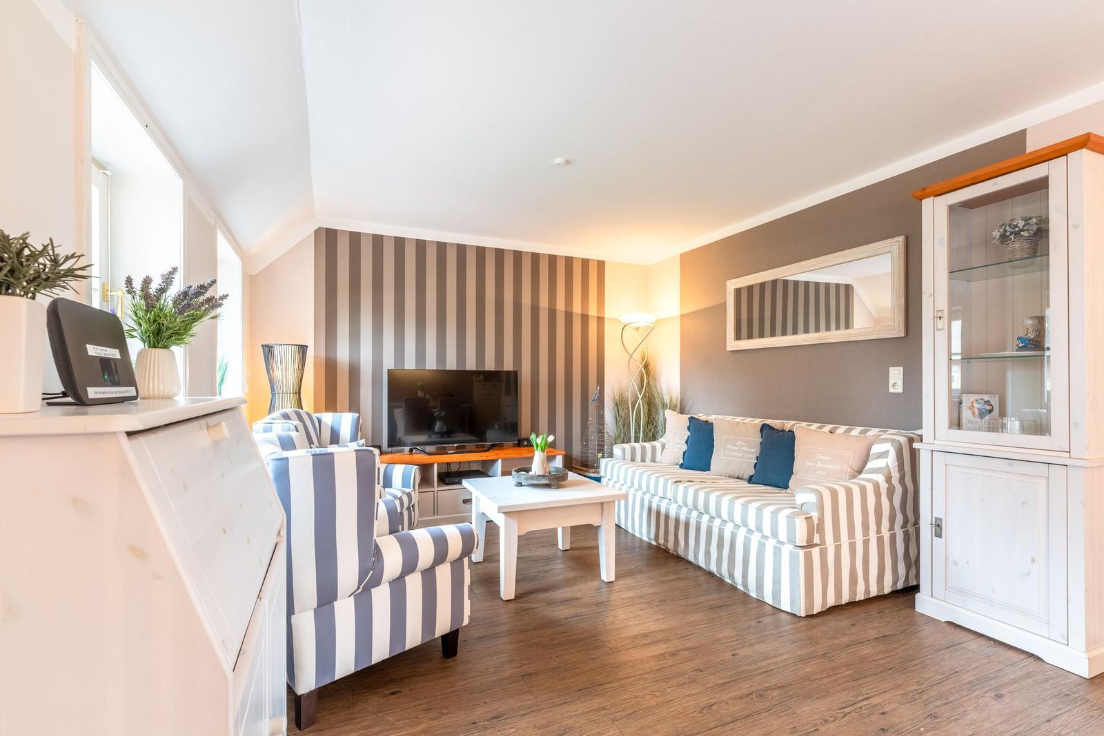 Wohnzimmer mit Sofa, Sessel und Fernseher. Holzboden und gestreifter Wand.