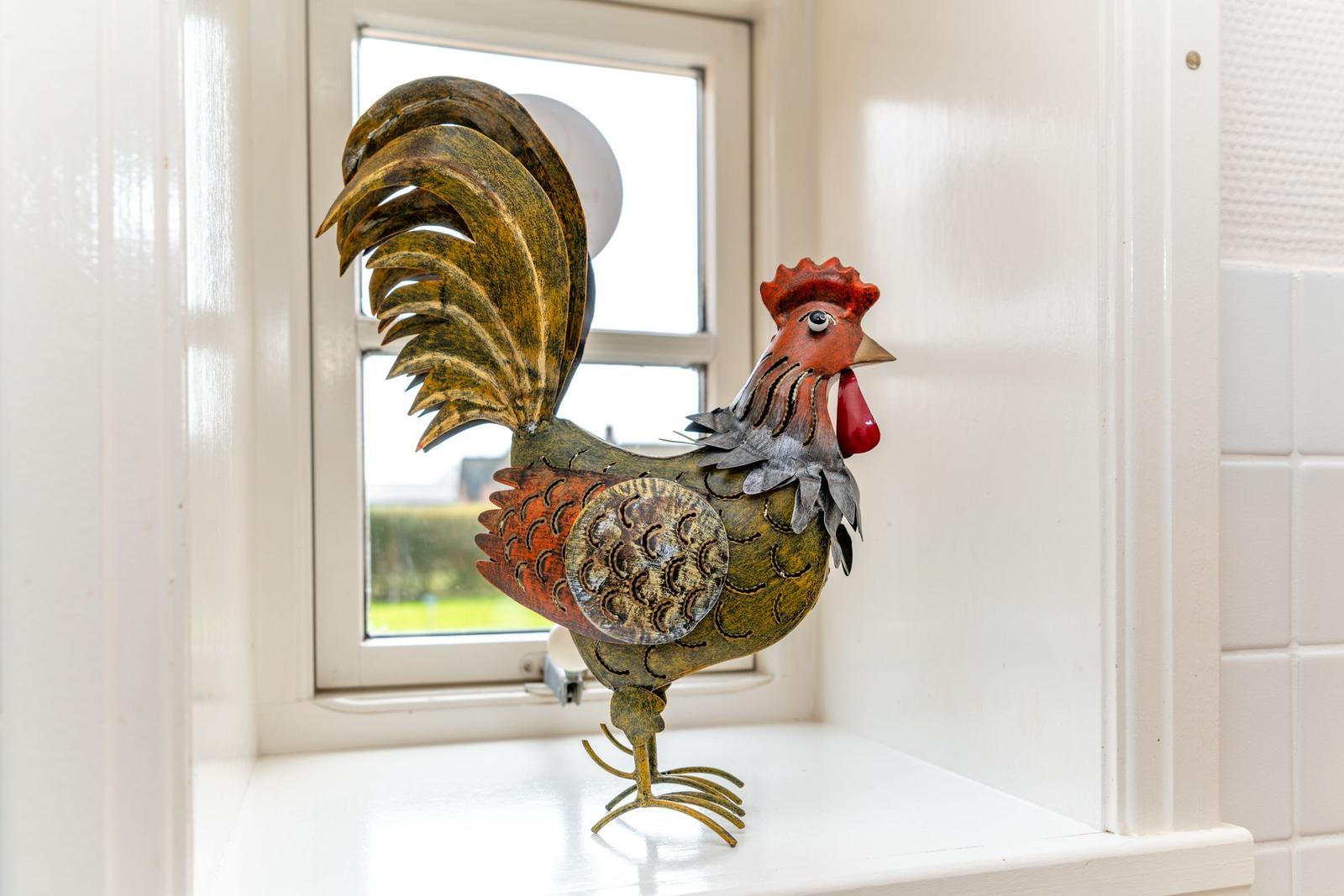 Metallfigur eines Hahns auf Fensterbank