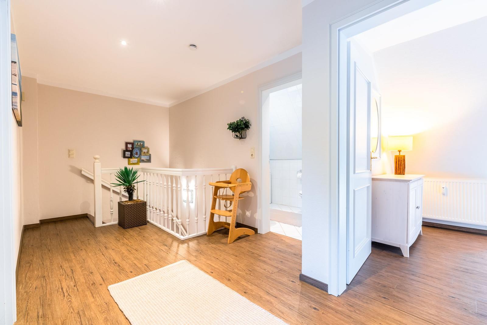 Haus mit Holzboden, weißen Wänden und Kindersitz. Flur führt in Bad und Schlafzimmer.