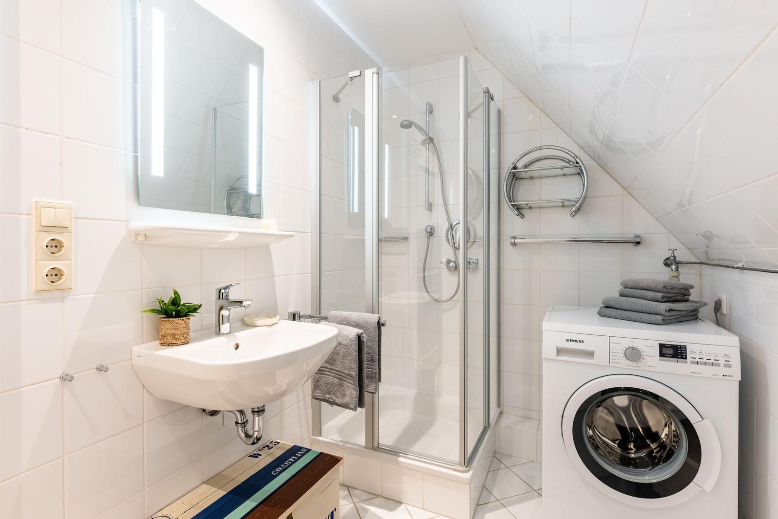 Badezimmer mit Dusche, Waschmaschine und Spiegel mit Beleuchtung.