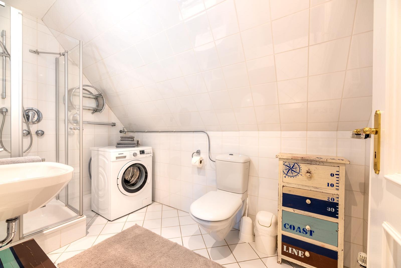Badezimmer mit Dusche, Waschmaschine, Toilette und Küchenzeile.