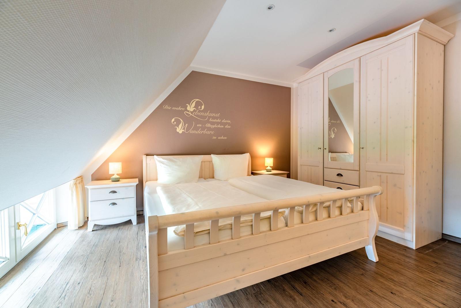 Schlafzimmer mit Doppelbett, Kleiderschrank und Nachttischen unter Dachschrägen.