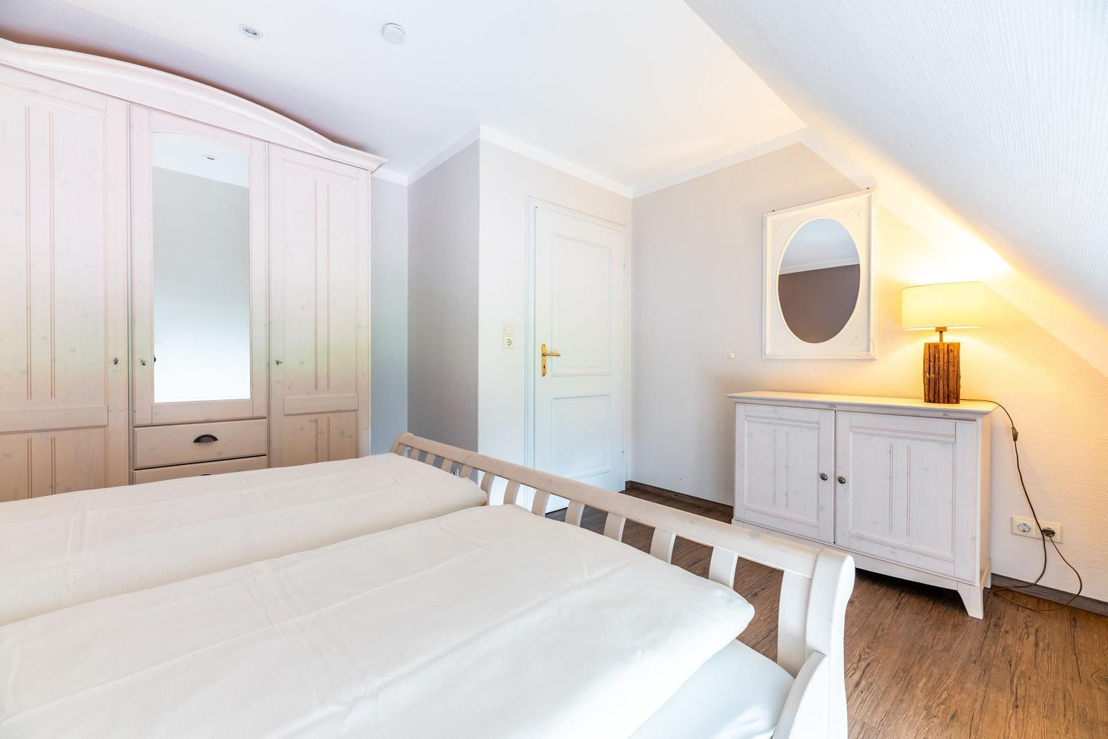 Schlafzimmer mit Doppelbett, Kleiderschrank und Schminktisch unter Dachschrägen.