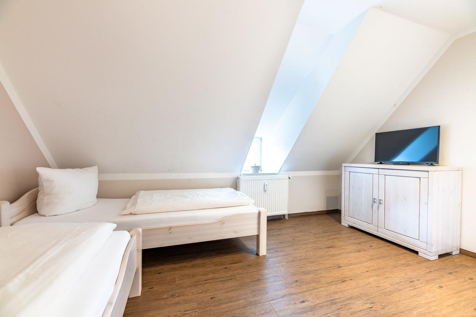 Zimmer mit Dachschrägen, Bett, TV-Schrank und Fenster.