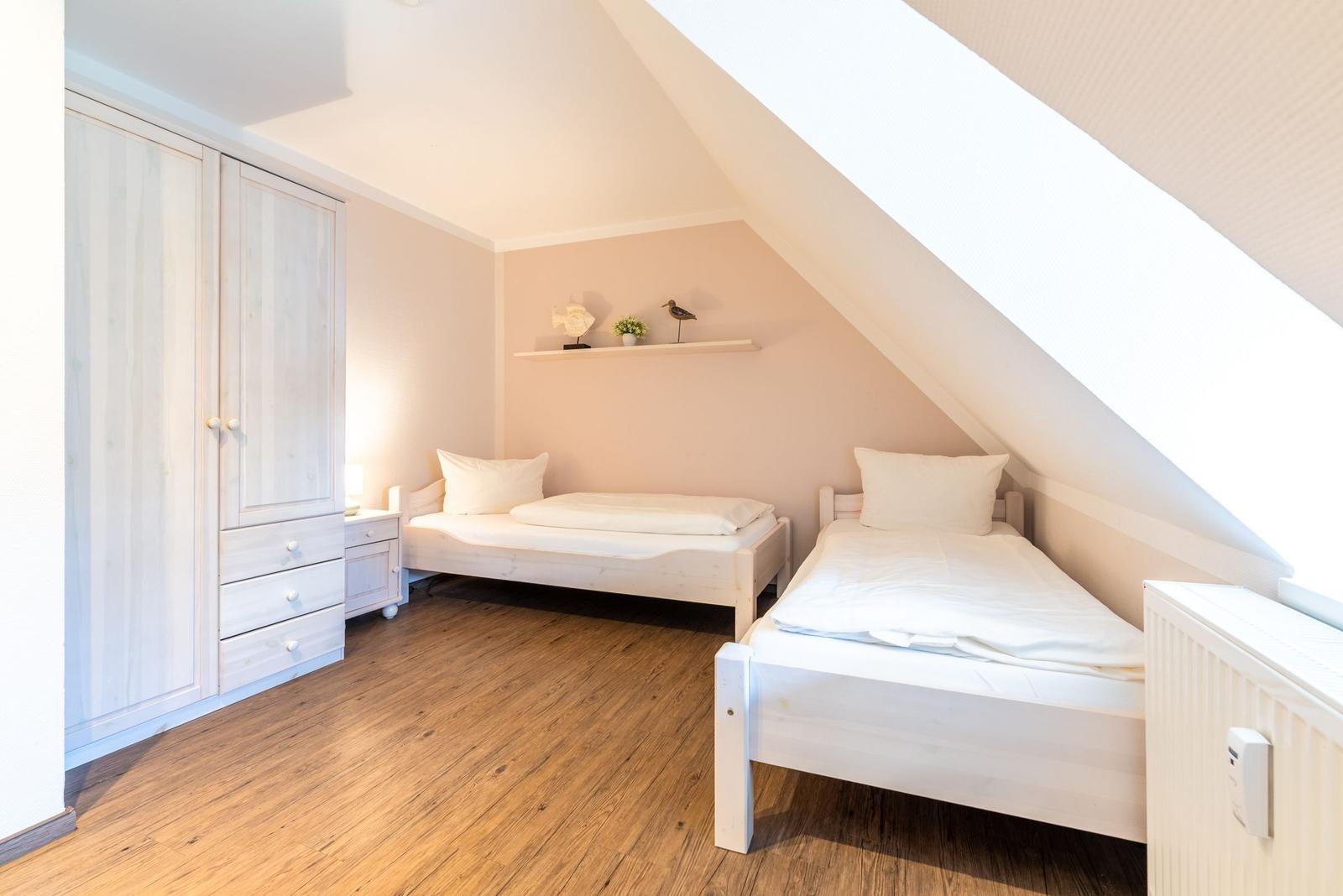Zwei Einzelbetten, Kleiderschrank und Holzboden in einem Dachzimmer.