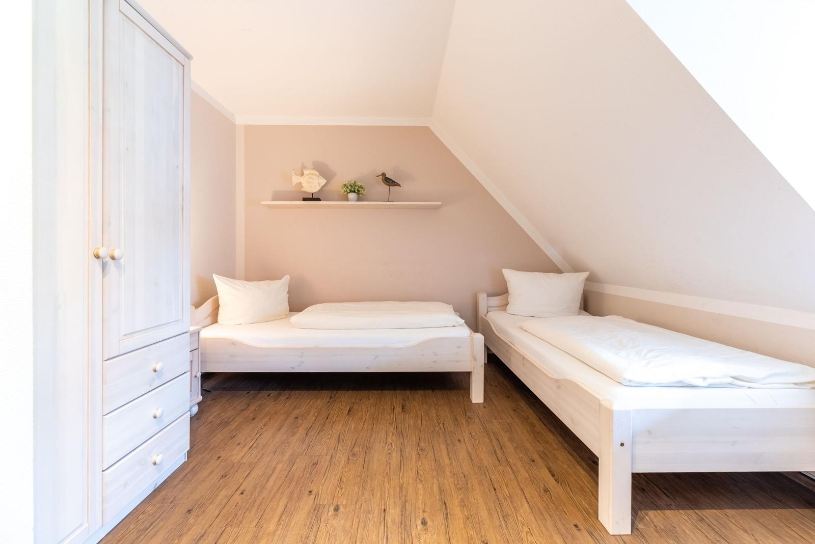 Zimmer mit zwei Betten, Holzboden und Kleiderschrank unter schräger Decke.