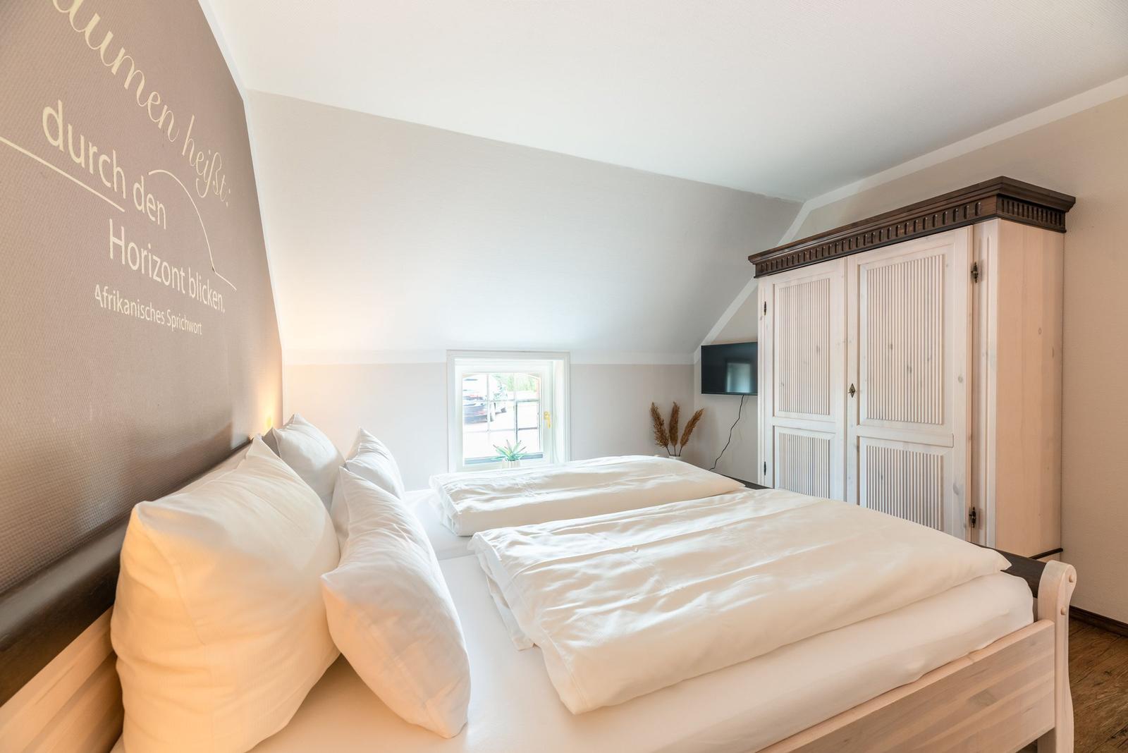 Schlafzimmer mit Doppelbett, Kleiderschrank und Fenster. Wand mit afrikanischem Sprichwort.