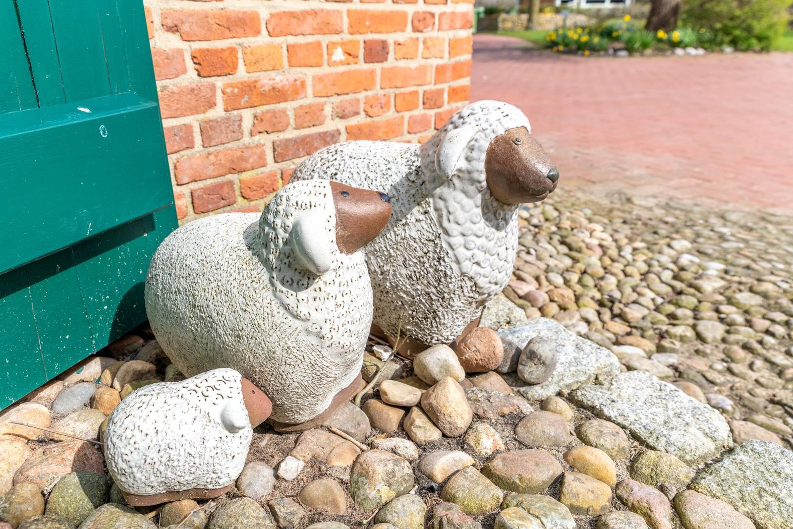 Drei Schafskulpturen stehen vor einer Backsteinmauer auf Kies.