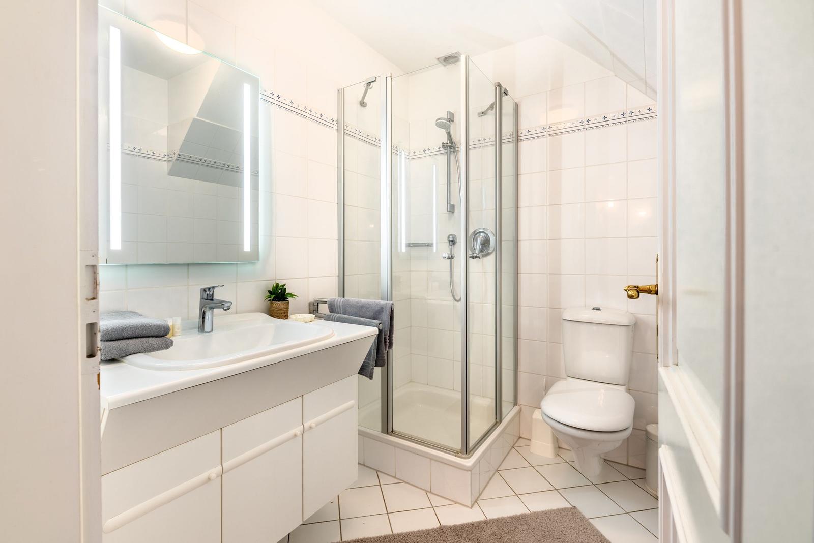 Badezimmer mit Dusche, Waschbecken und Toilette. Weiße Fliesen und Spiegelschrank.