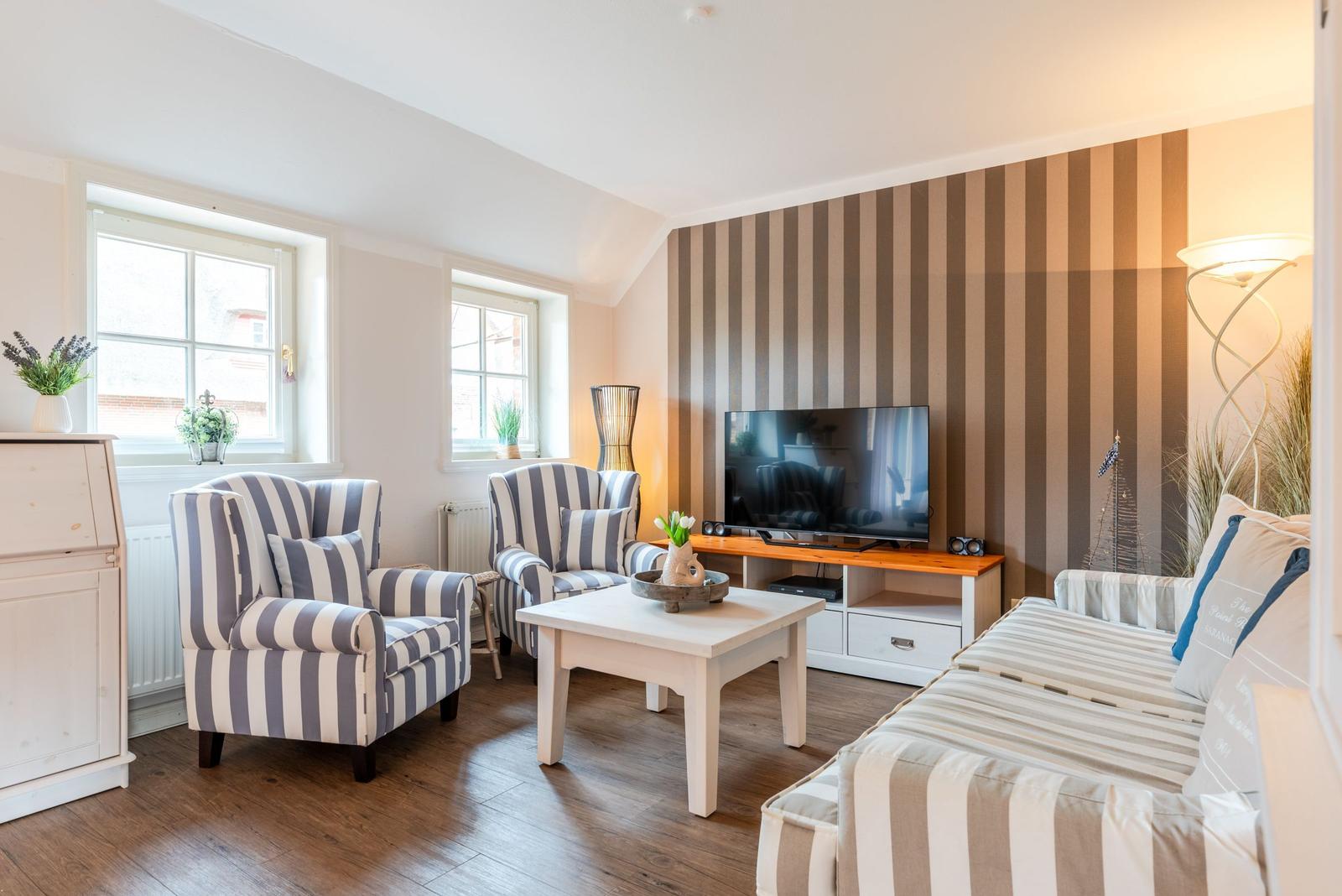 Wohnzimmer mit gestreiften Sitzmöbeln, Fernseher und Holzboden.