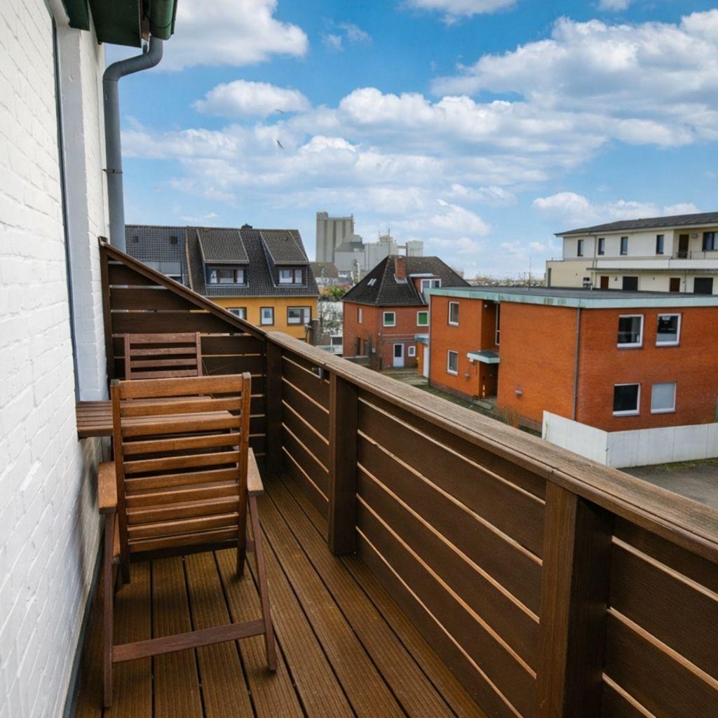 Holzterrasse mit Stuhl, Blick auf Wohnhäuser und blauen Himmel.