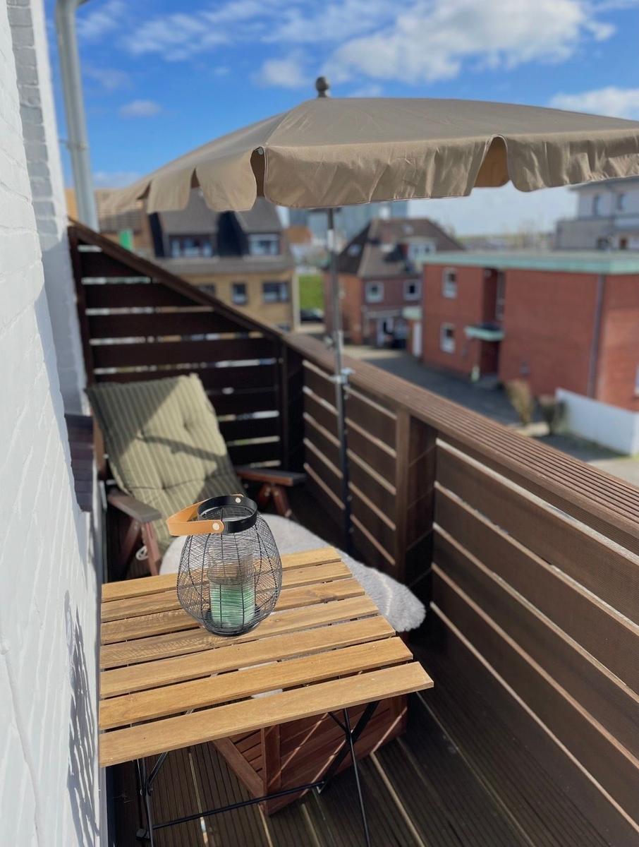 Terrasse mit Holztisch, Sonnenschirm und Liegestuhl. Blick auf Wohngebiet.