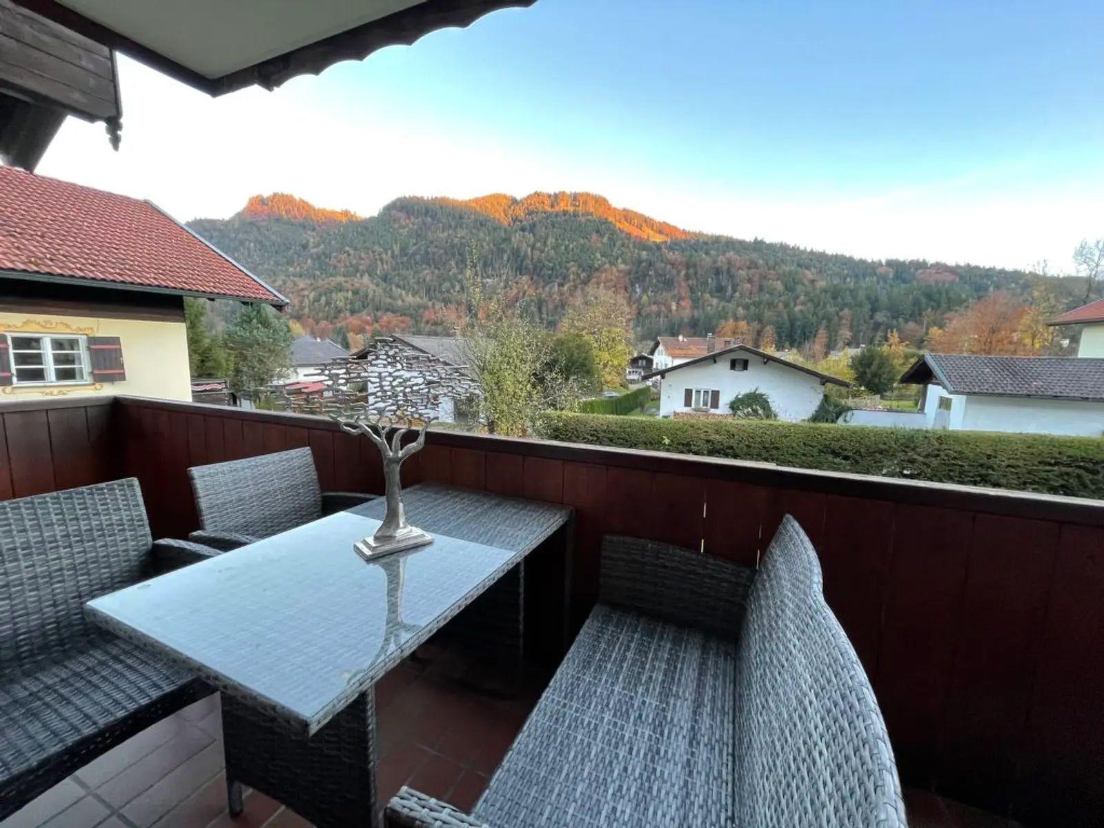 Terrasse mit Tisch und Stühlen. Blick auf Hügel mit Wald und Häusern.