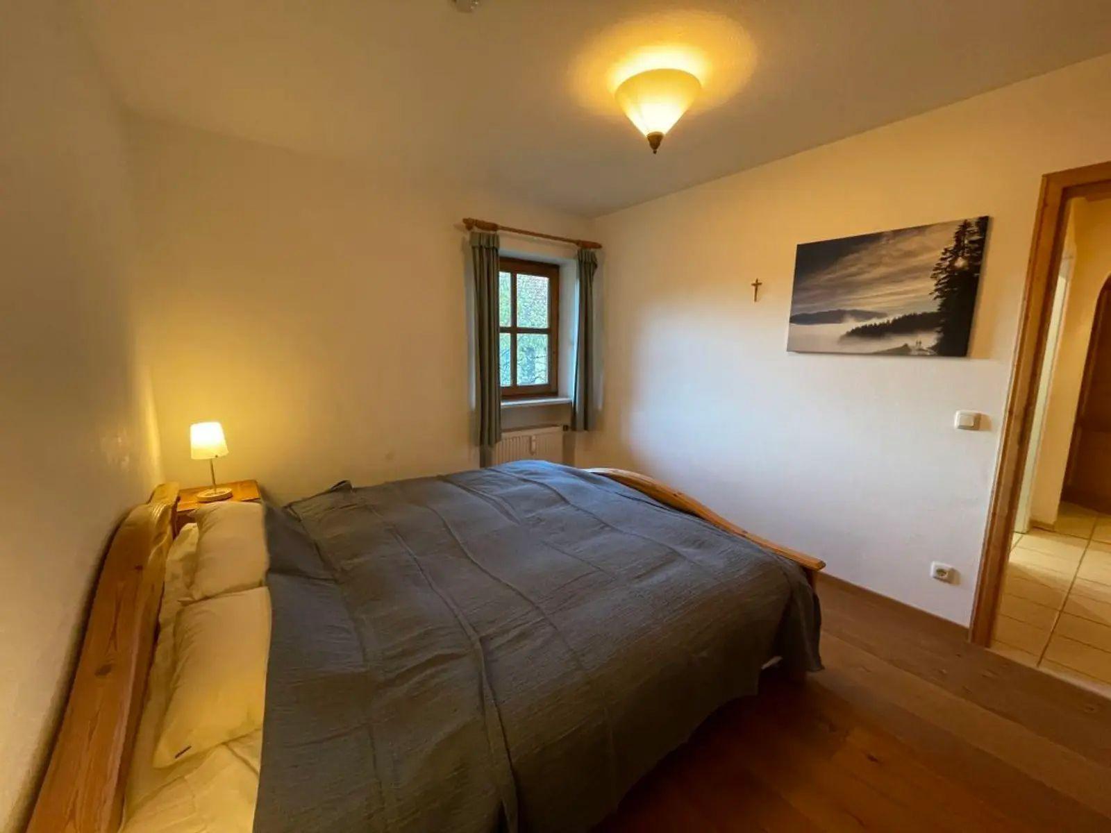 Ein Schlafzimmer mit Holzbett, Fenster, Lampe und Wandbild.
