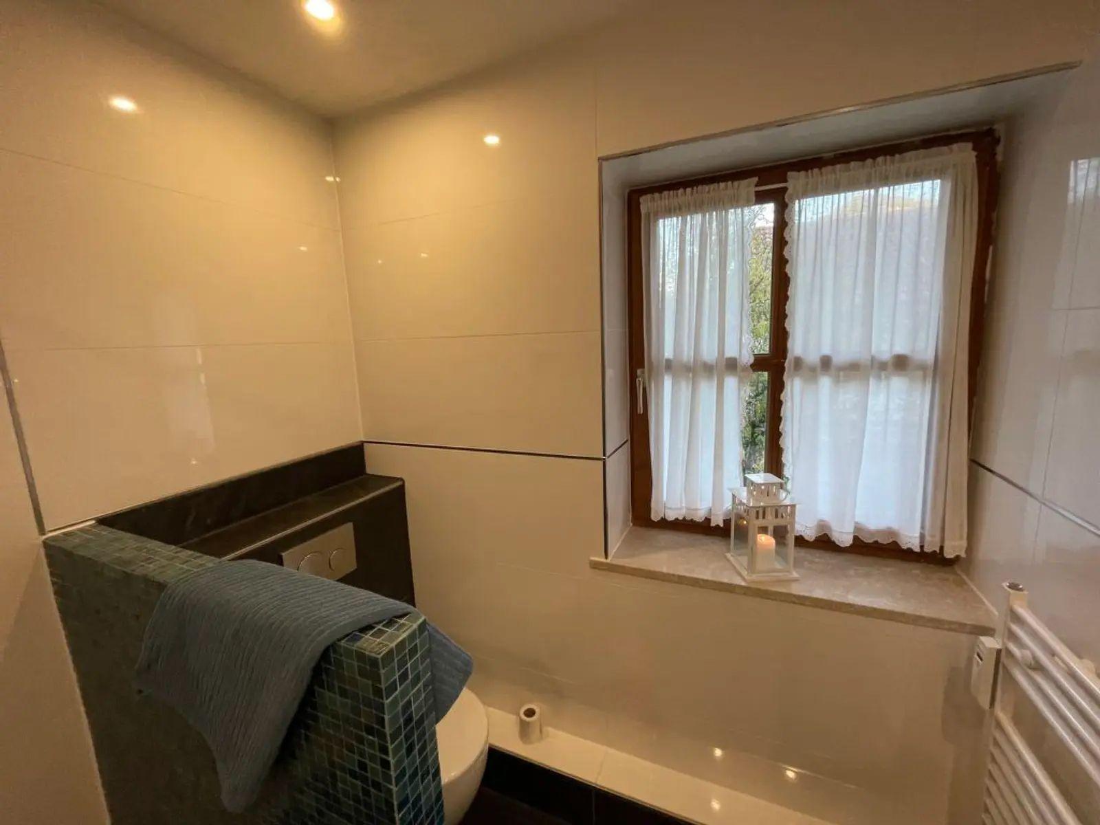 Bad mit Fenster, Toilette und Badewanne. Auf dem Fensterbrett steht eine Laterne mit Kerze.