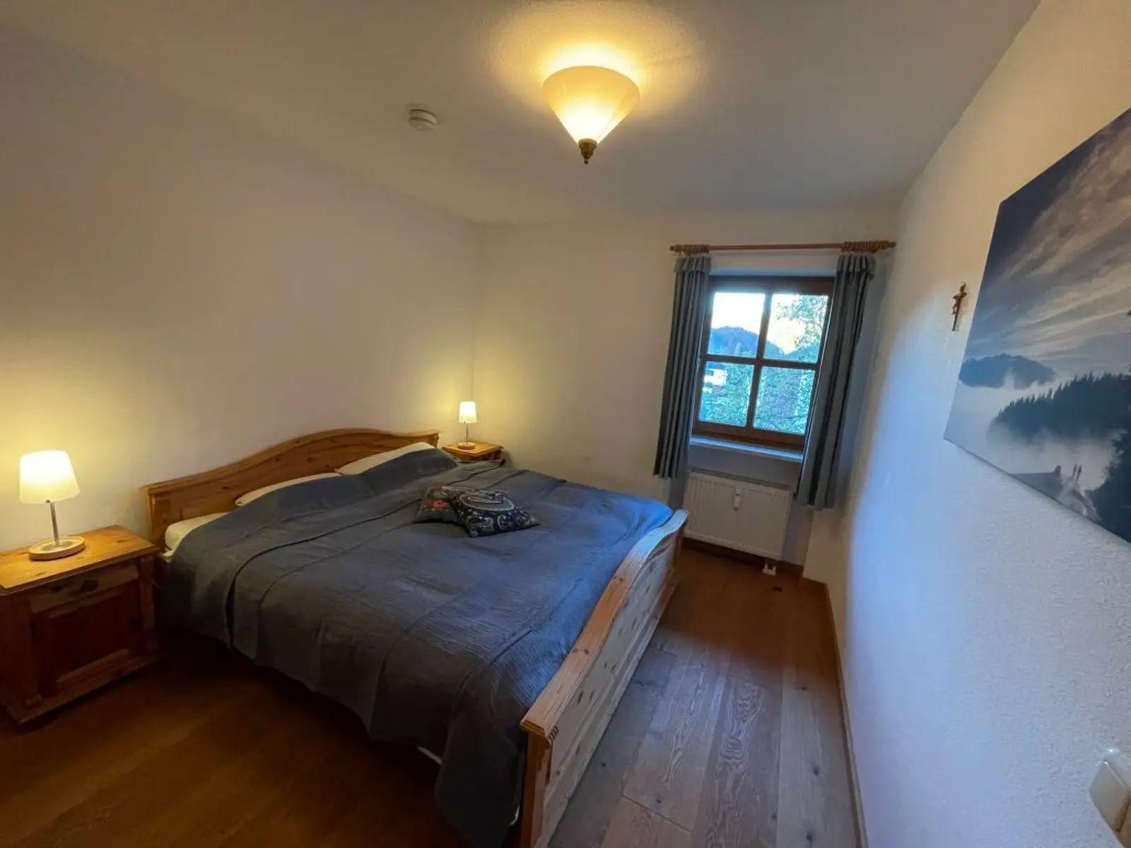 Schlafzimmer mit Holzbett, Nachttischen und Fenster mit Blick auf die Berge.