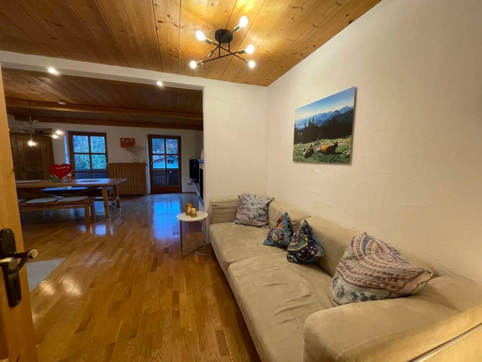 Wohnzimmer mit Sofa, Kissen und Holzboden. Wandbild zeigt Berglandschaft.