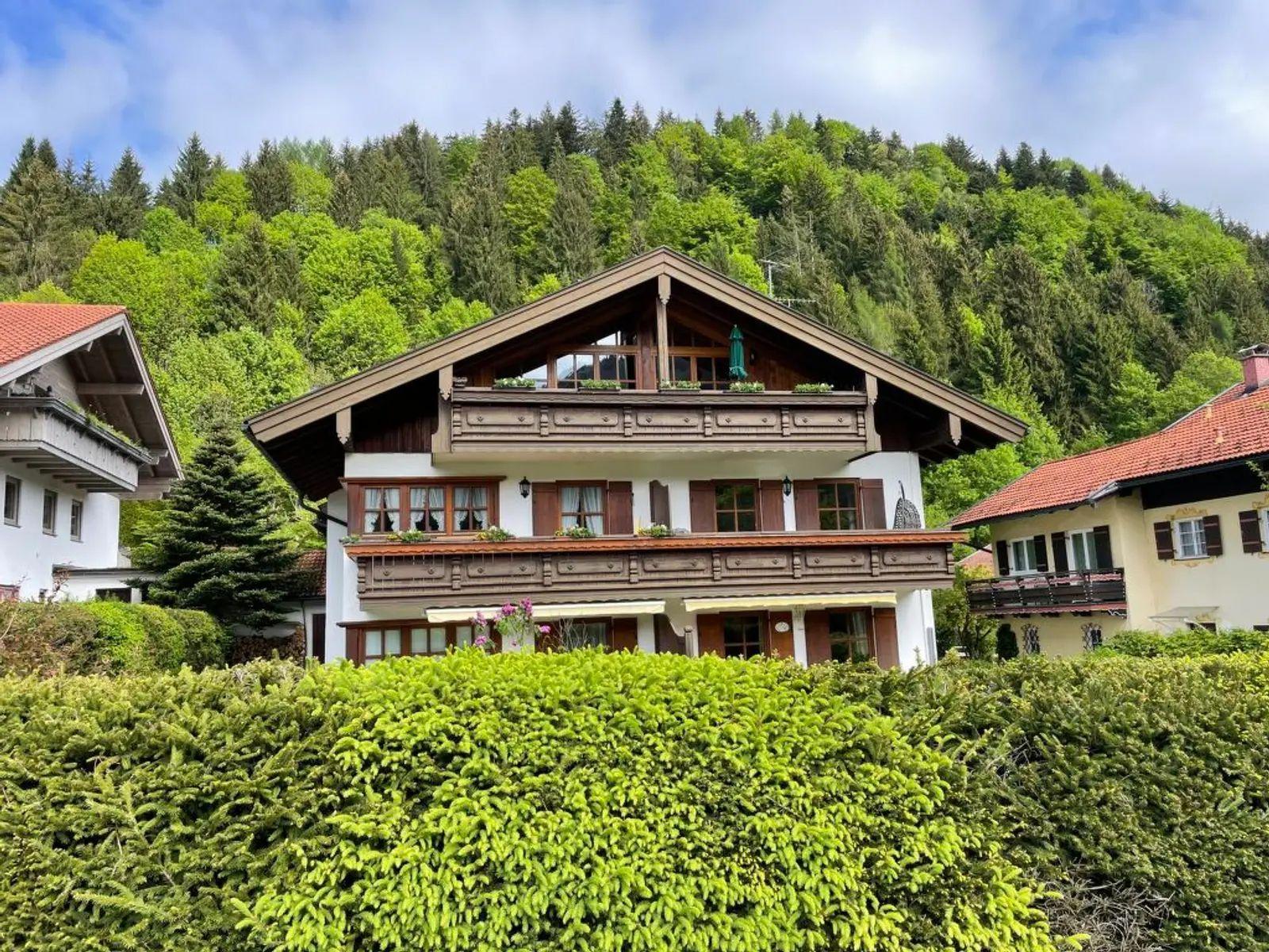 Ein zweistöckiges Haus mit Balkon und rotem Dach, umgeben von grünen Hedges und einem Waldhintergrund.