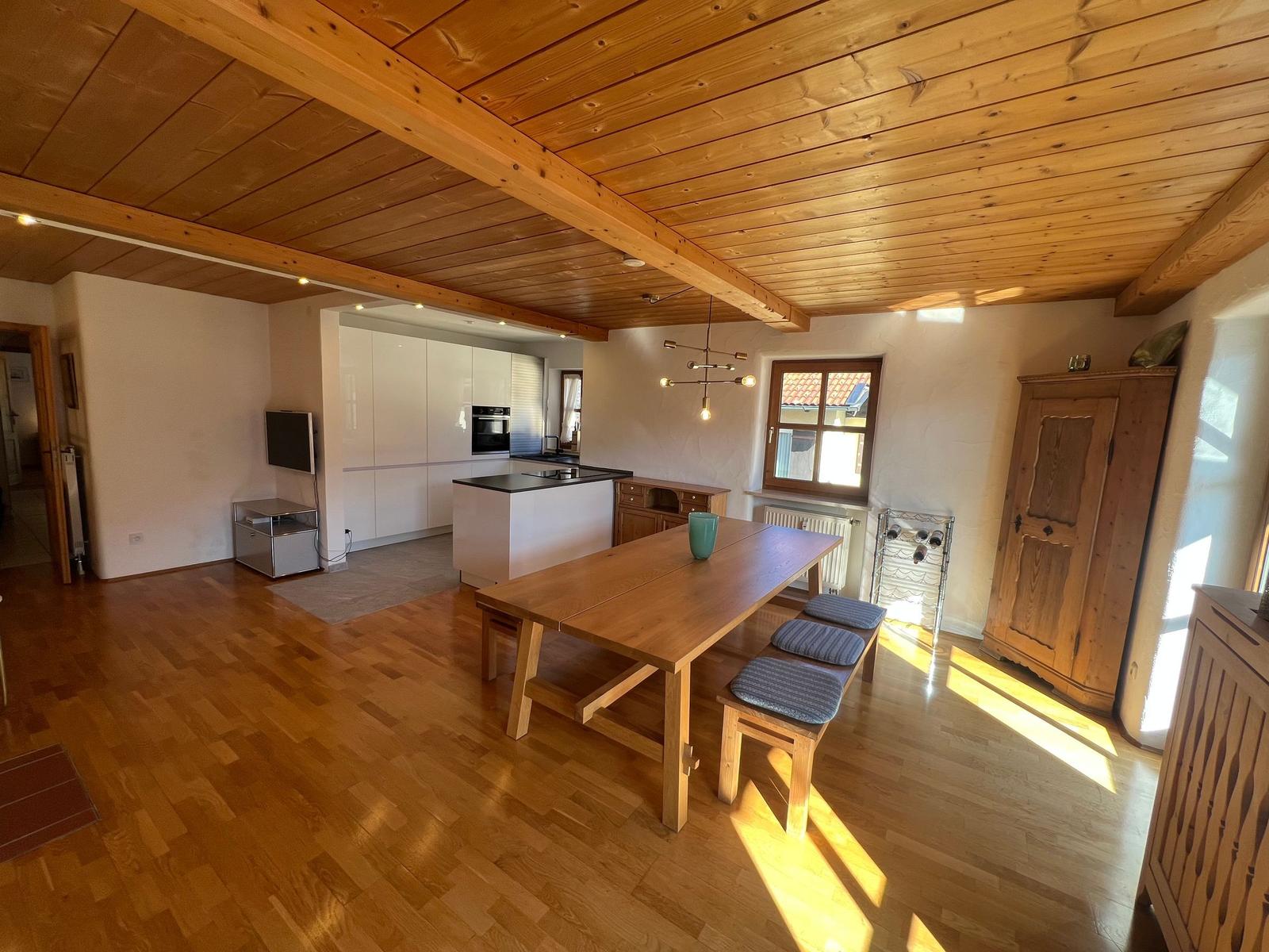 Großes Esszimmer mit Holztisch und Bänken, Küche im Hintergrund, Holzdecke und Parkettboden.