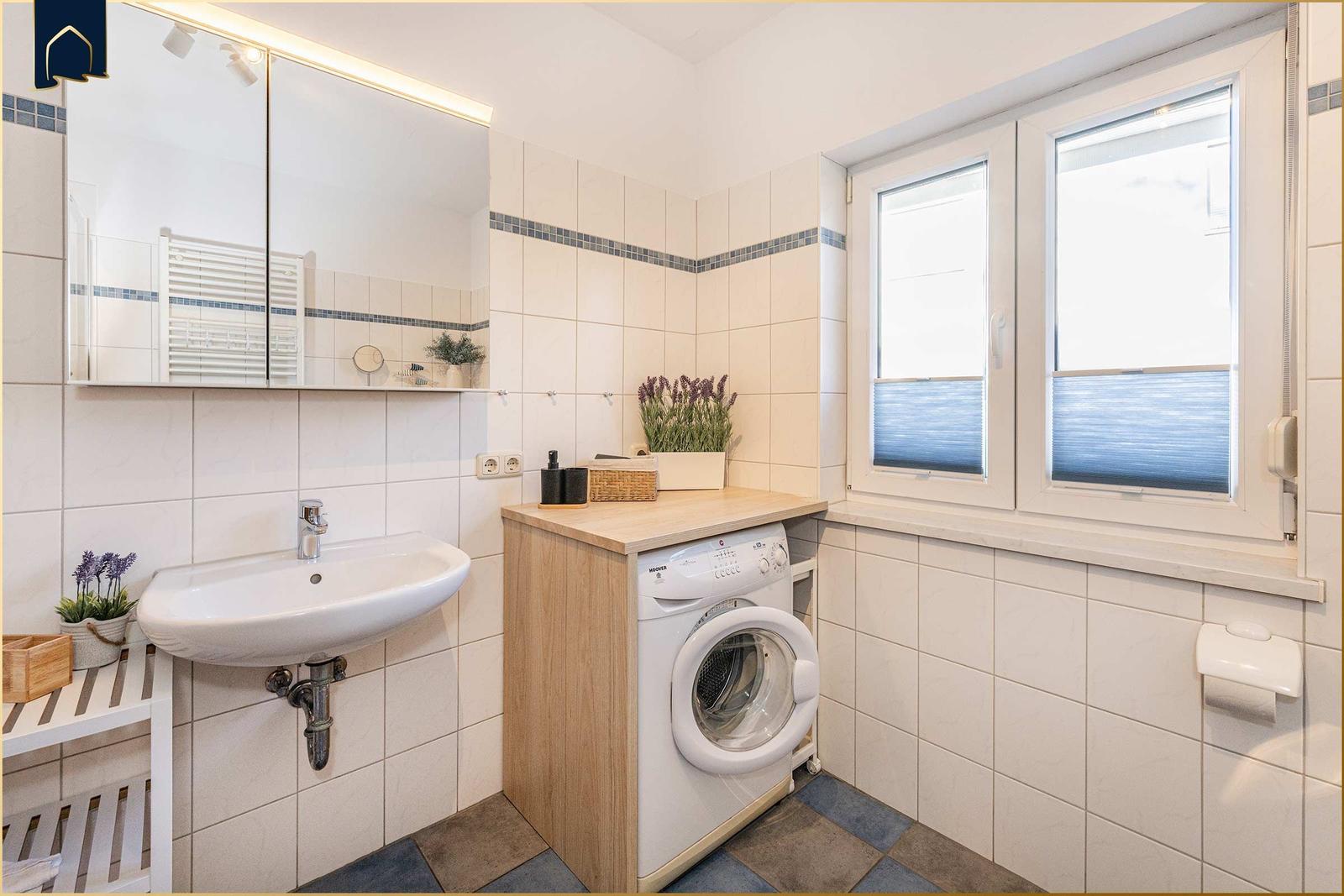 Badezimmer mit Waschmaschine, Spiegel und Fenster.