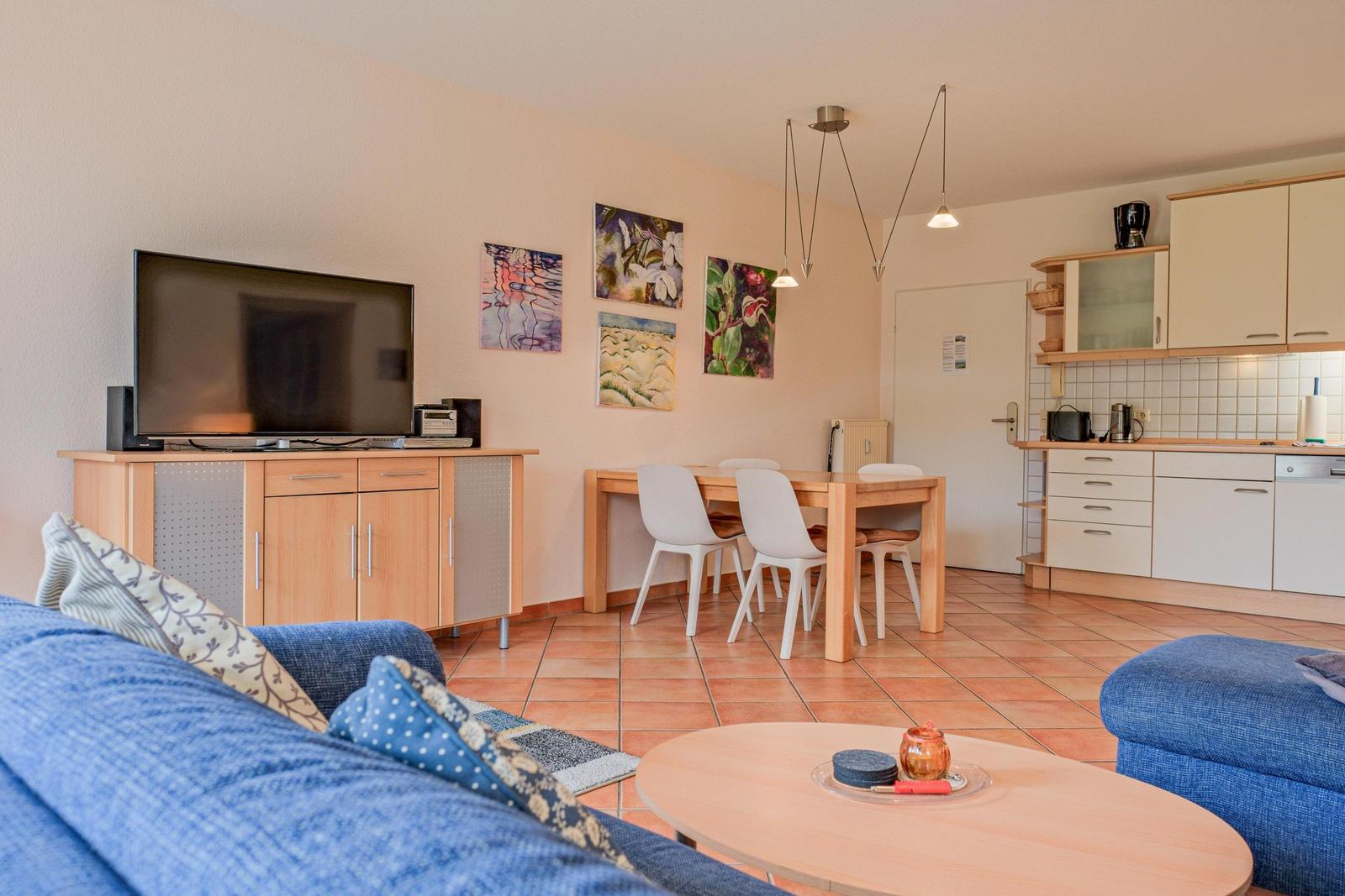 Wohn- und Essbereich mit Küchenzeile, TV und Holztisch mit Stühlen.