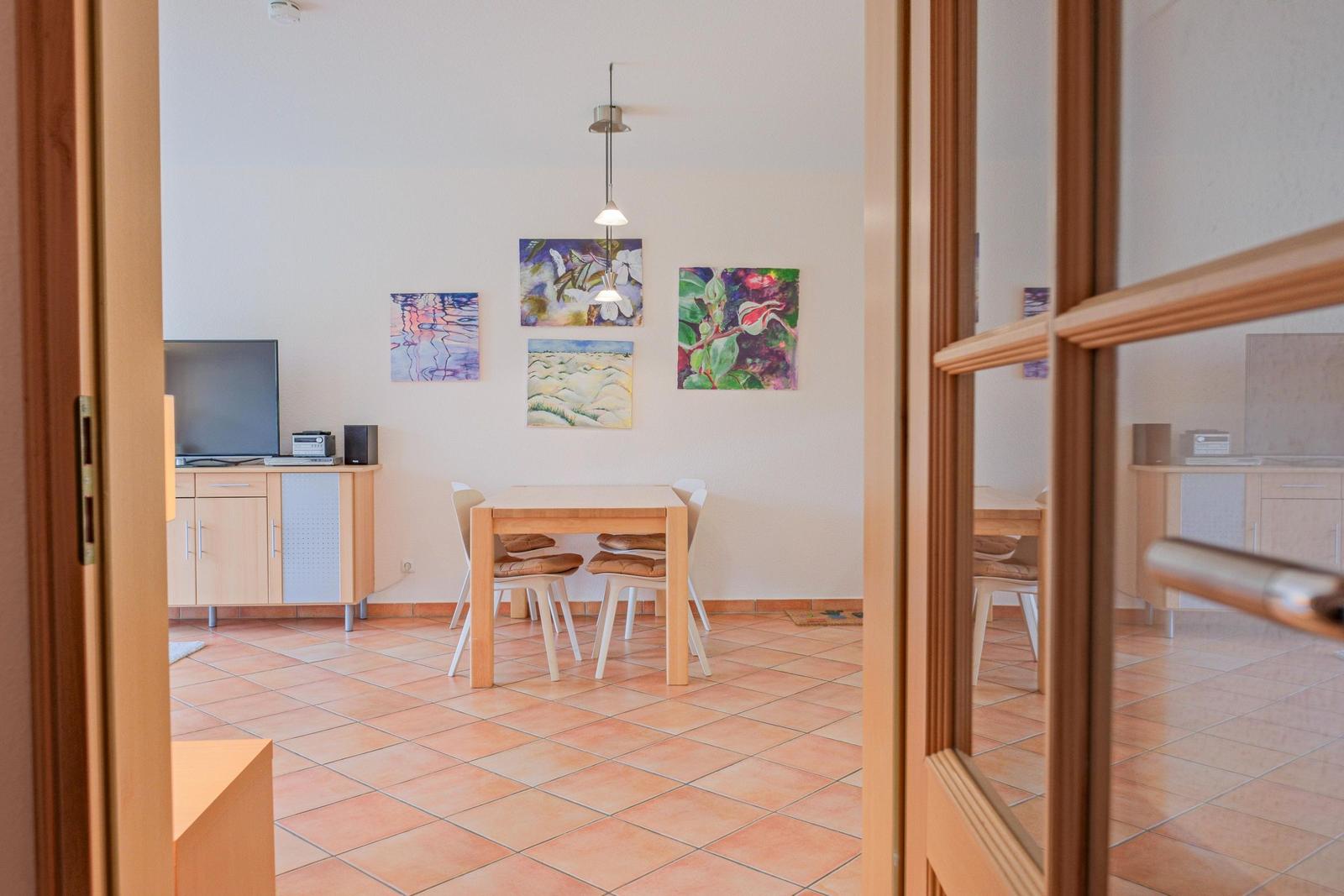 Essbereich mit Tisch, Stühlen und Wandbildern. Terrakottafußboden und Fernseher.