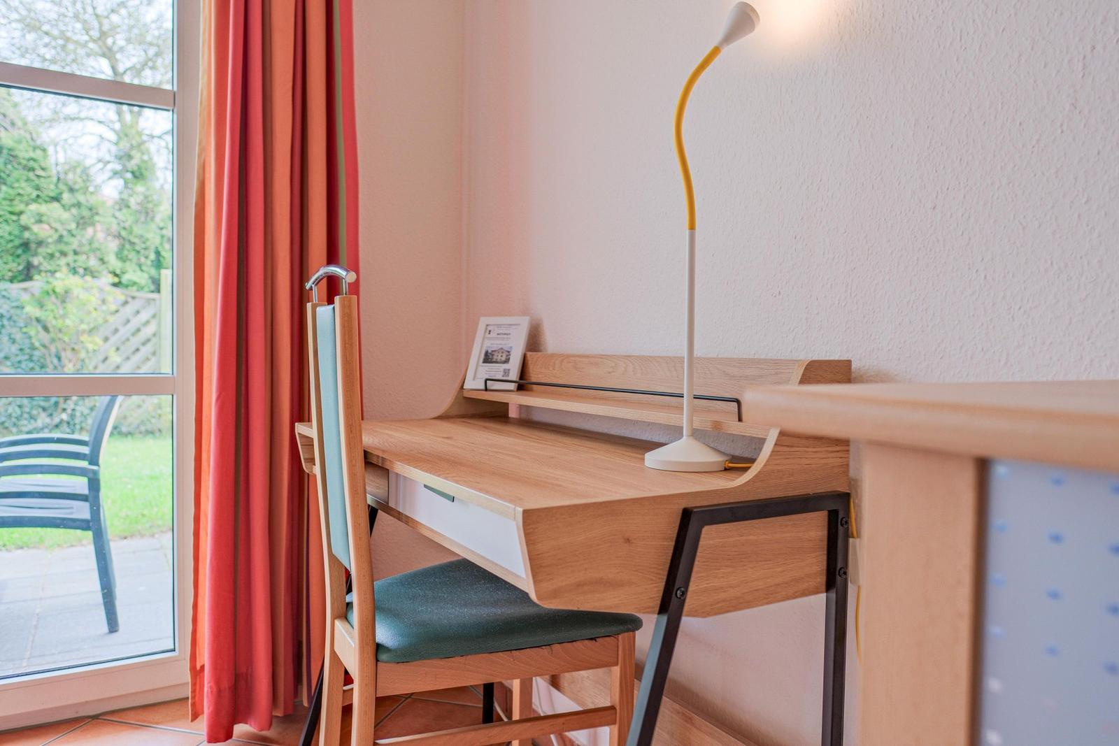 Schreibtisch mit Stuhl und Stehlampe neben Fenster mit Blick auf Garten