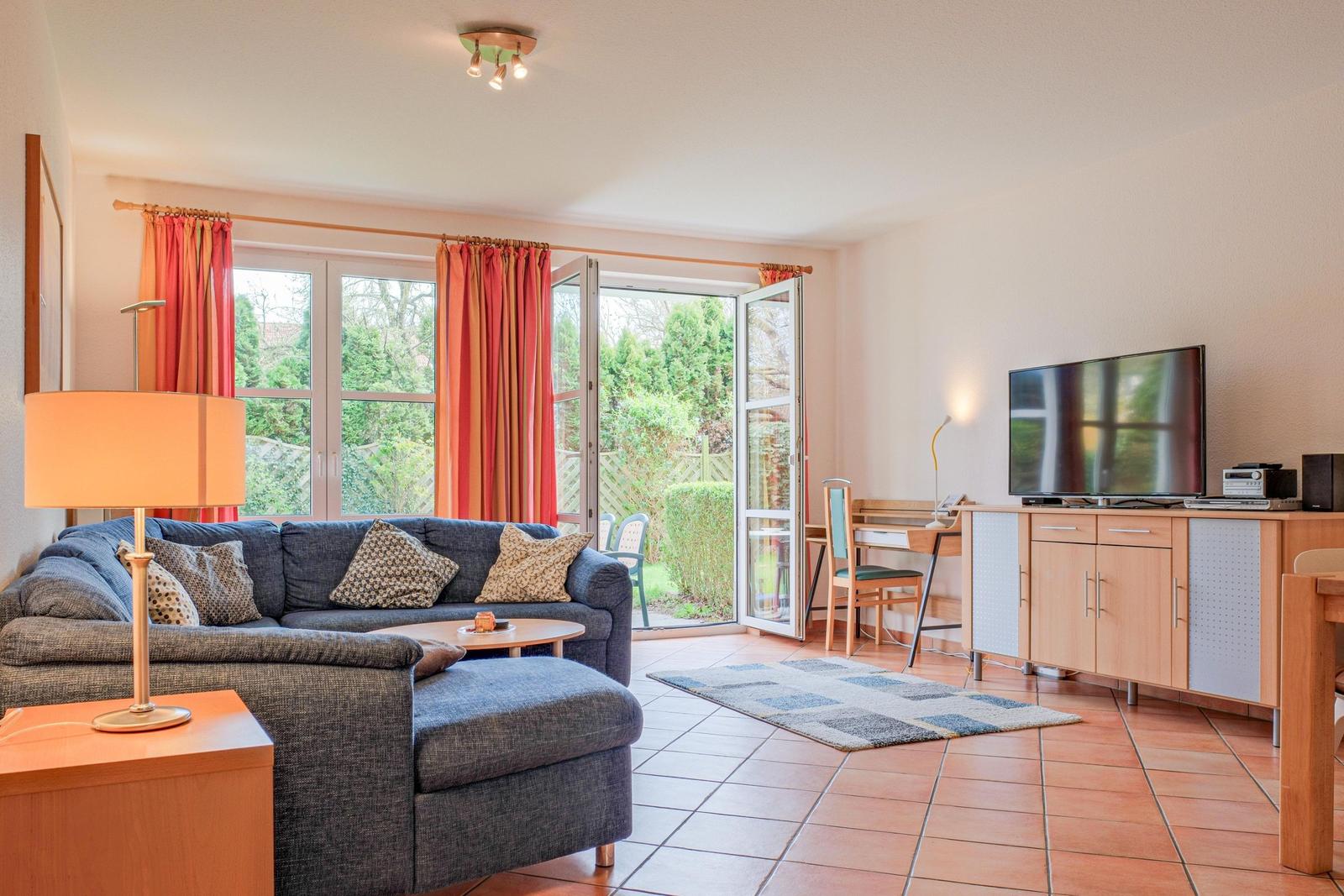 Wohnzimmer mit Sofa, Fernseher und Terrassentür. Blick auf Garten.