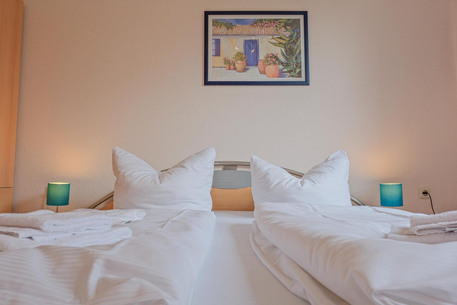 Zwei Betten mit weißen Laken, zwei Nachttische mit Lampen und ein Bild an der Wand.
