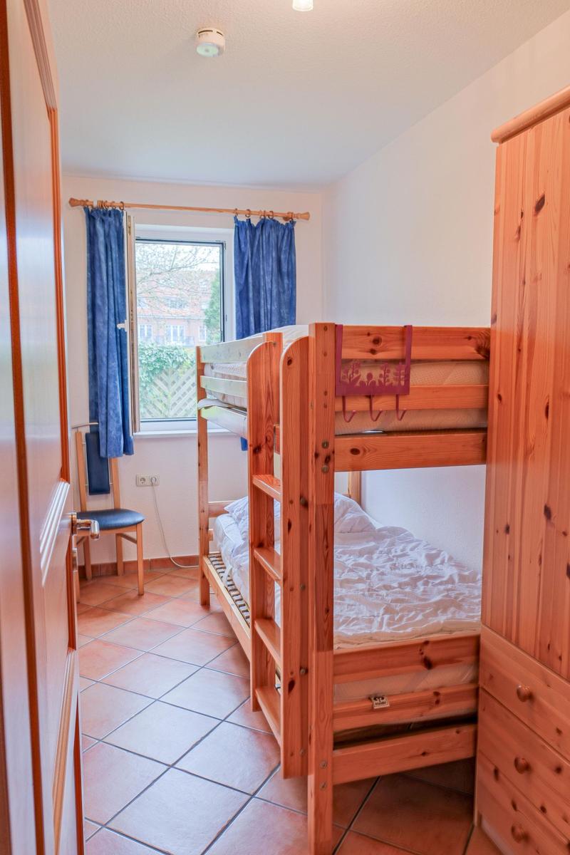 Zimmer mit Doppelstockbett, Holzschrank und Fenster mit blauen Vorhängen.