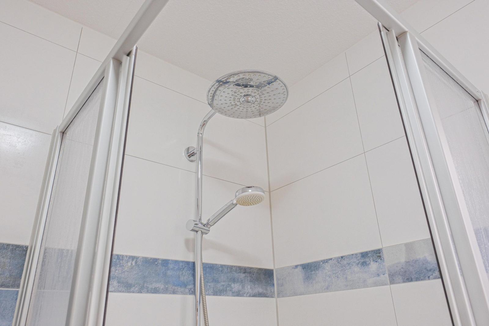 Dusche mit Duschbrause und Handbrause, weiße Fliesen mit blauer Zierleiste.