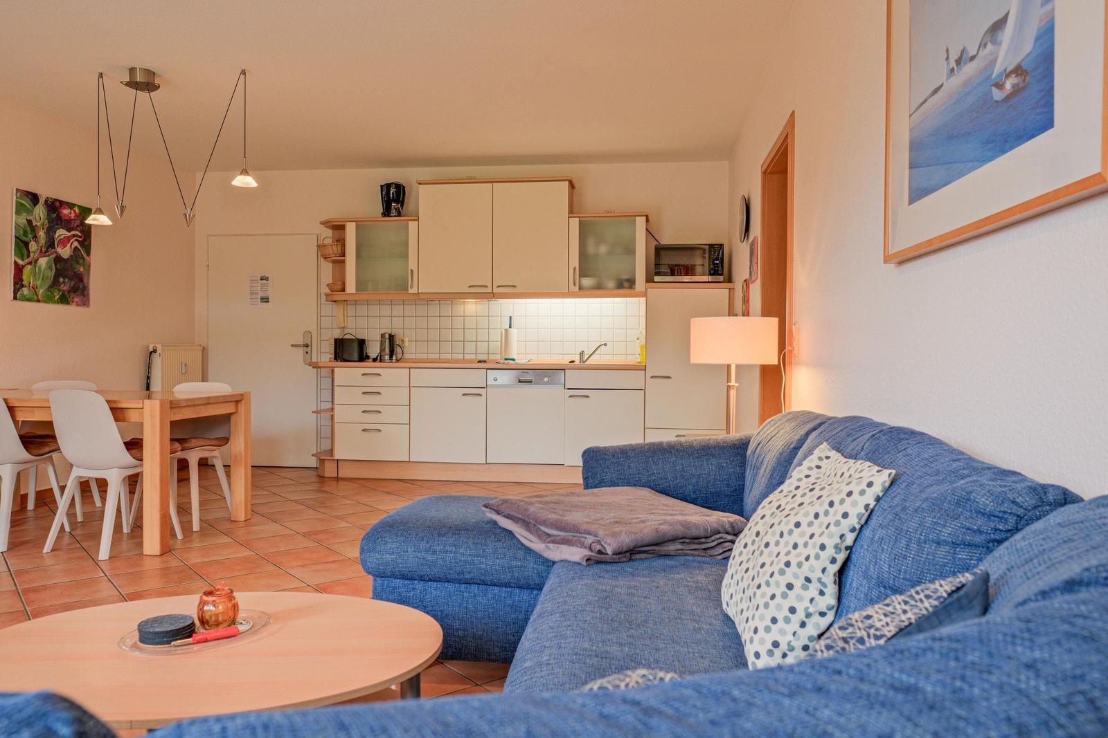 Wohnbereich mit blauem Sofa, Küchenzeile und Esstisch.