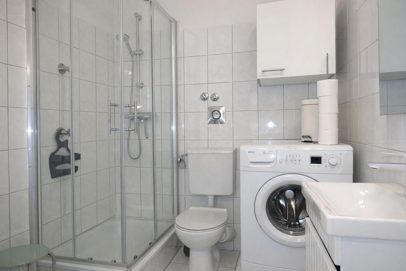 Badezimmer mit Dusche, Toilette, Waschmaschine und Waschtisch.