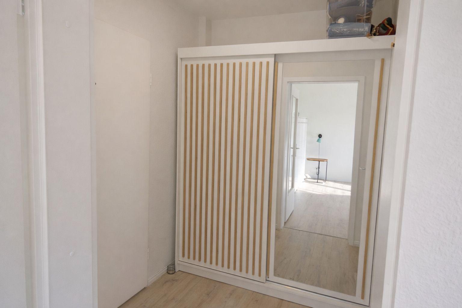 Schlafzimmer mit Schiebetüren und Spiegel. Holzfußboden und weiße Wände.