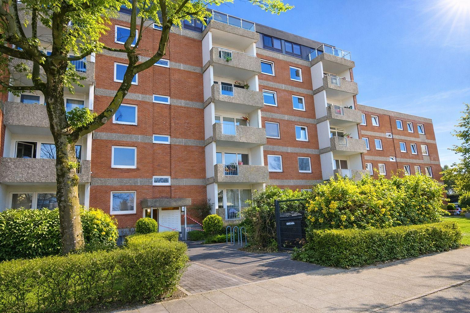 Mehrfamilienhaus mit Balkonen und grüner Umgebung unter blauem Himmel.