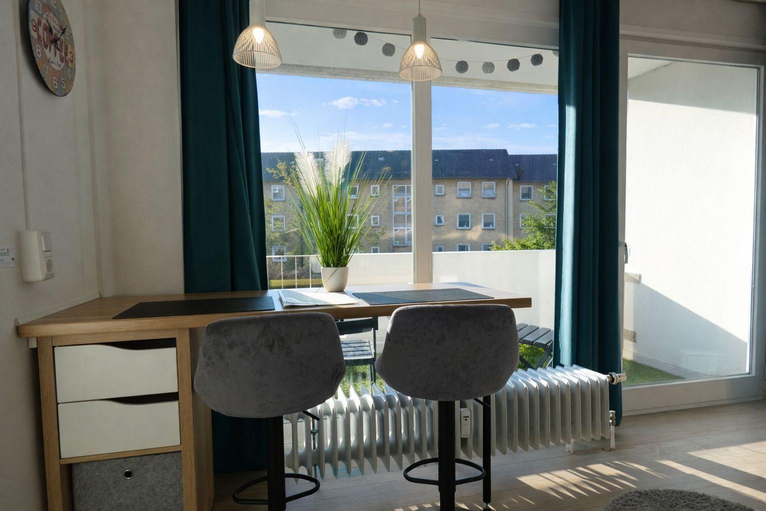 Esstisch mit zwei Stühlen vor großem Fenster mit Blick auf Balkon und Gebäude.