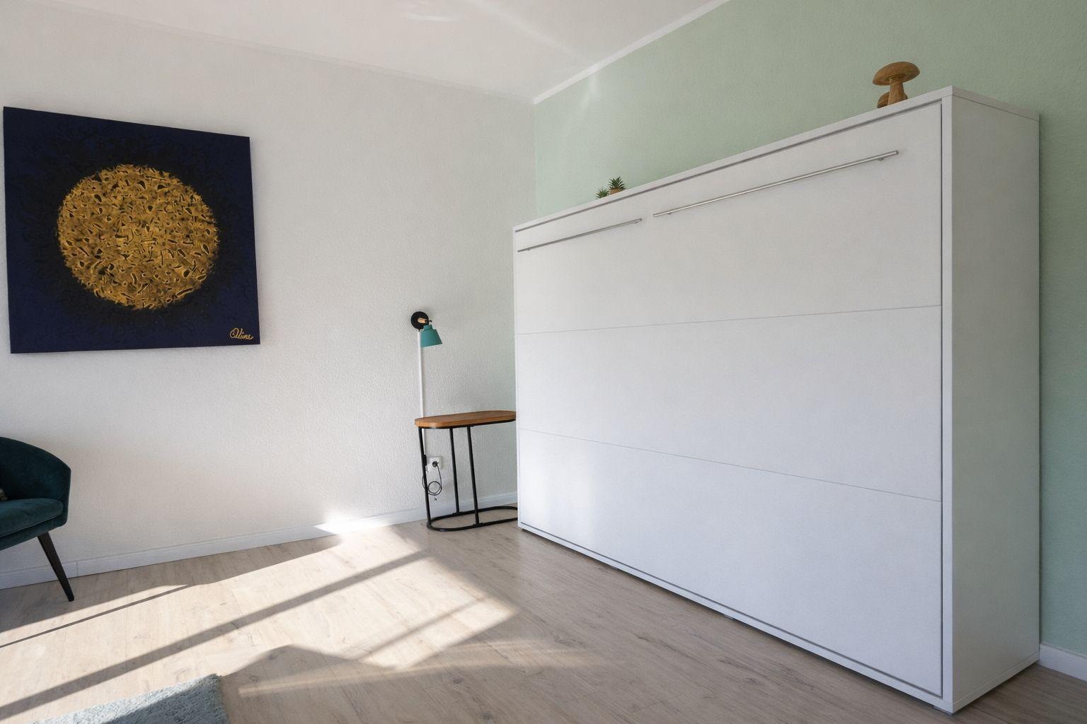 Ein Raum mit weißem Schrank, Wandbild und Holzboden.
