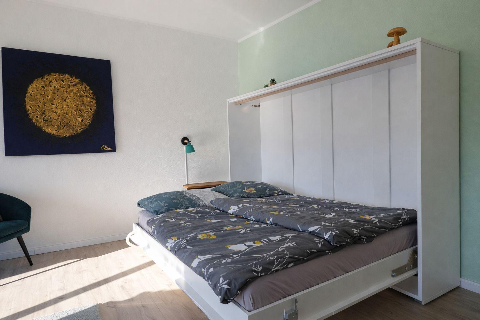 Schlafzimmer mit Bett, Wandbild und Schrank. Holzboden und grüne Wand.