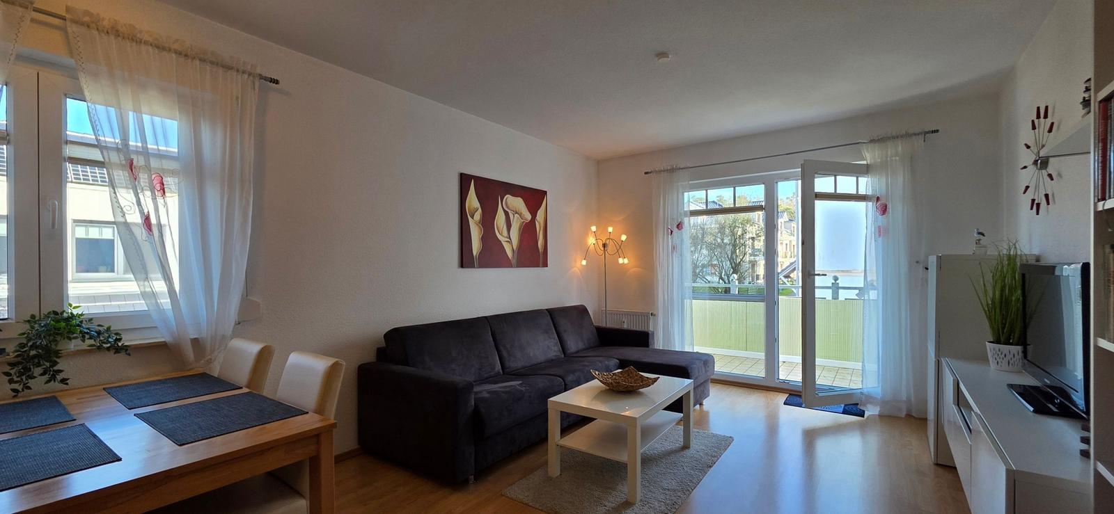 Wohn- und Essbereich mit Sofa, Tisch und Balkontür.