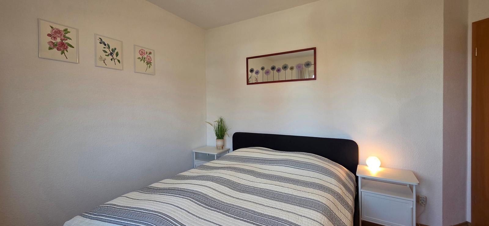 Schlafzimmer mit Bett, Nachttisch und Wandbildern.