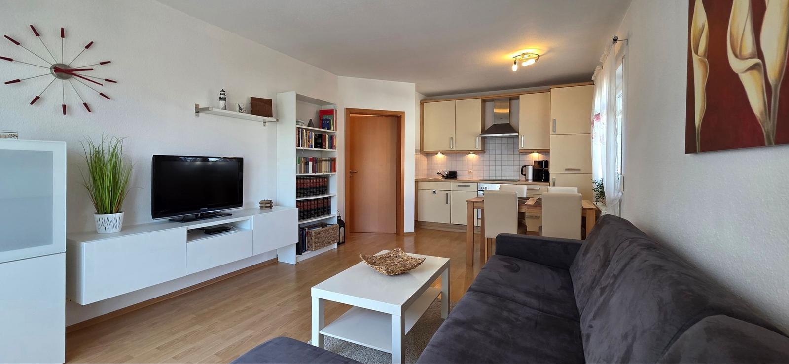 Wohnbereich mit Sofa, TV und Küchenbereich im Hintergrund.