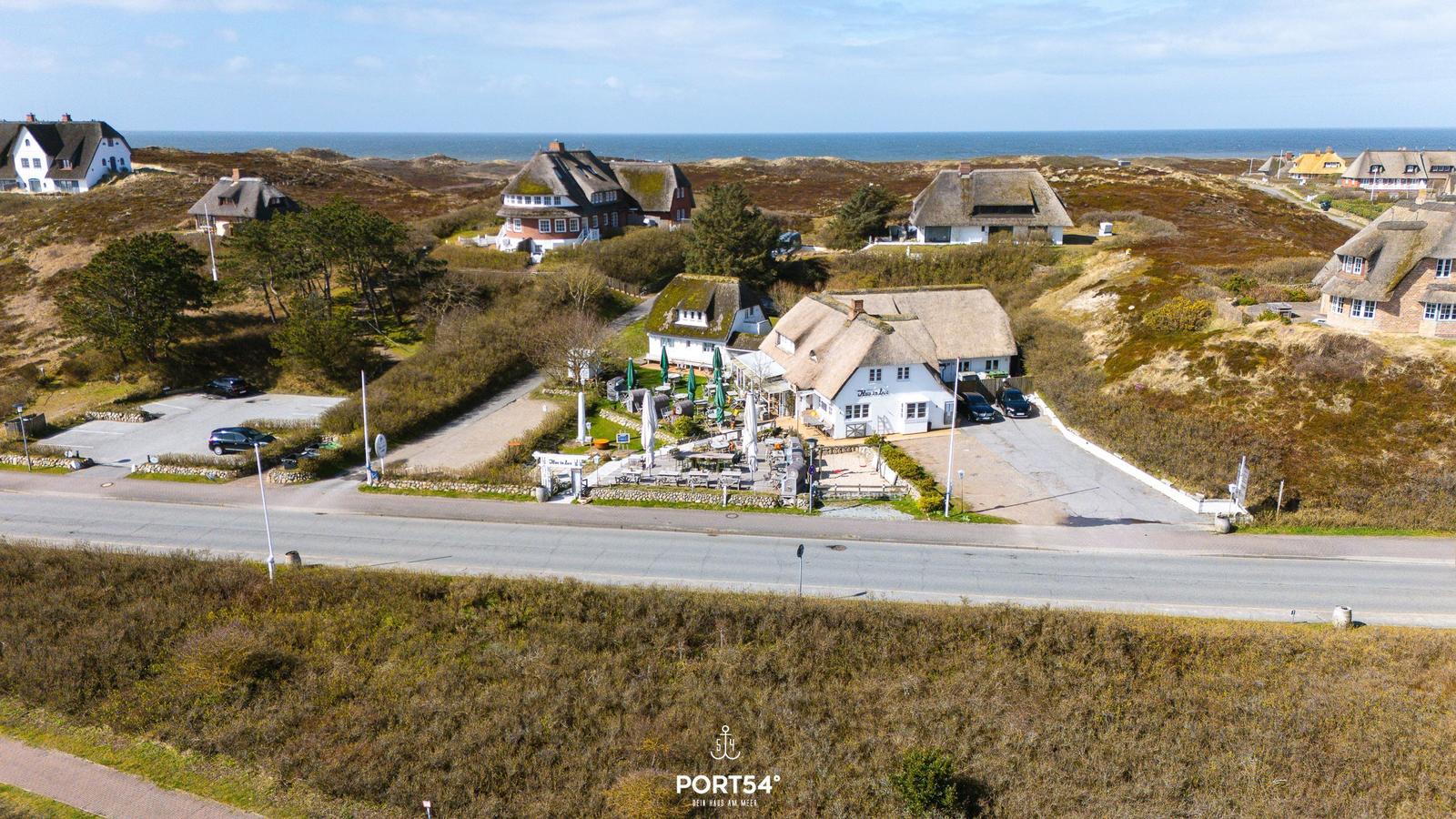 Haus mit Terrasse und Grillplatz an der Küste. Blick auf das Meer und umliegende Gebäude.
