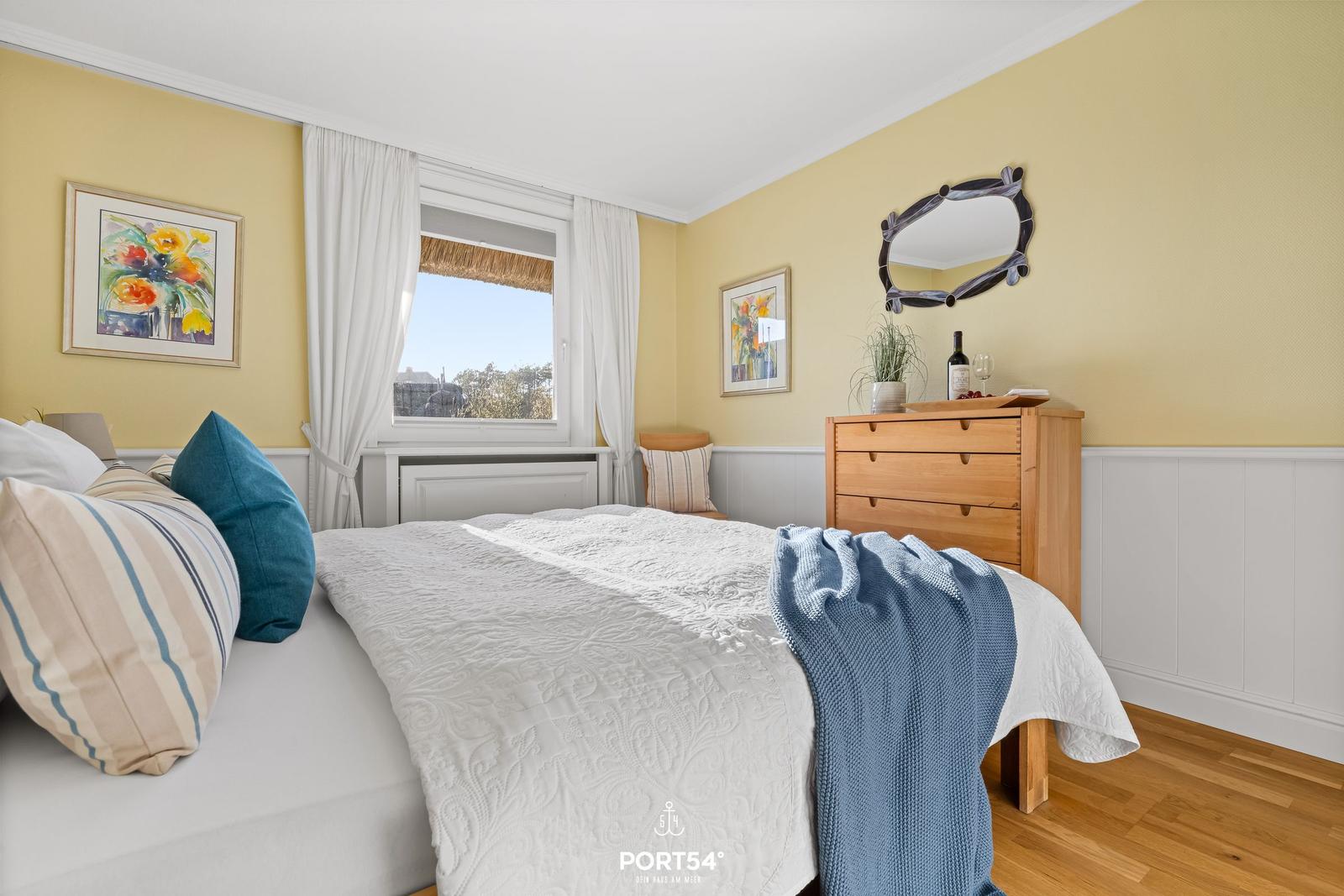 Schlafzimmer mit Bett, Schrank und Fenster. Gelbe Wände und Holzboden.