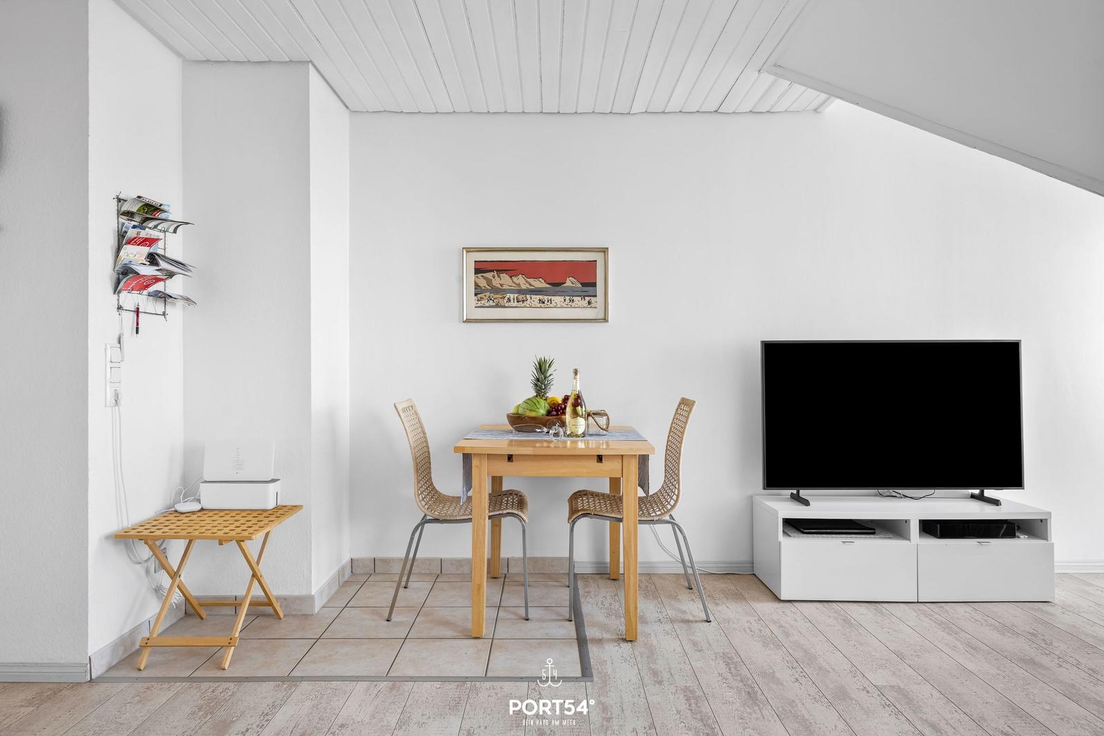 Essbereich mit Tisch, zwei Stühlen und Fernseher auf weißem Sideboard.