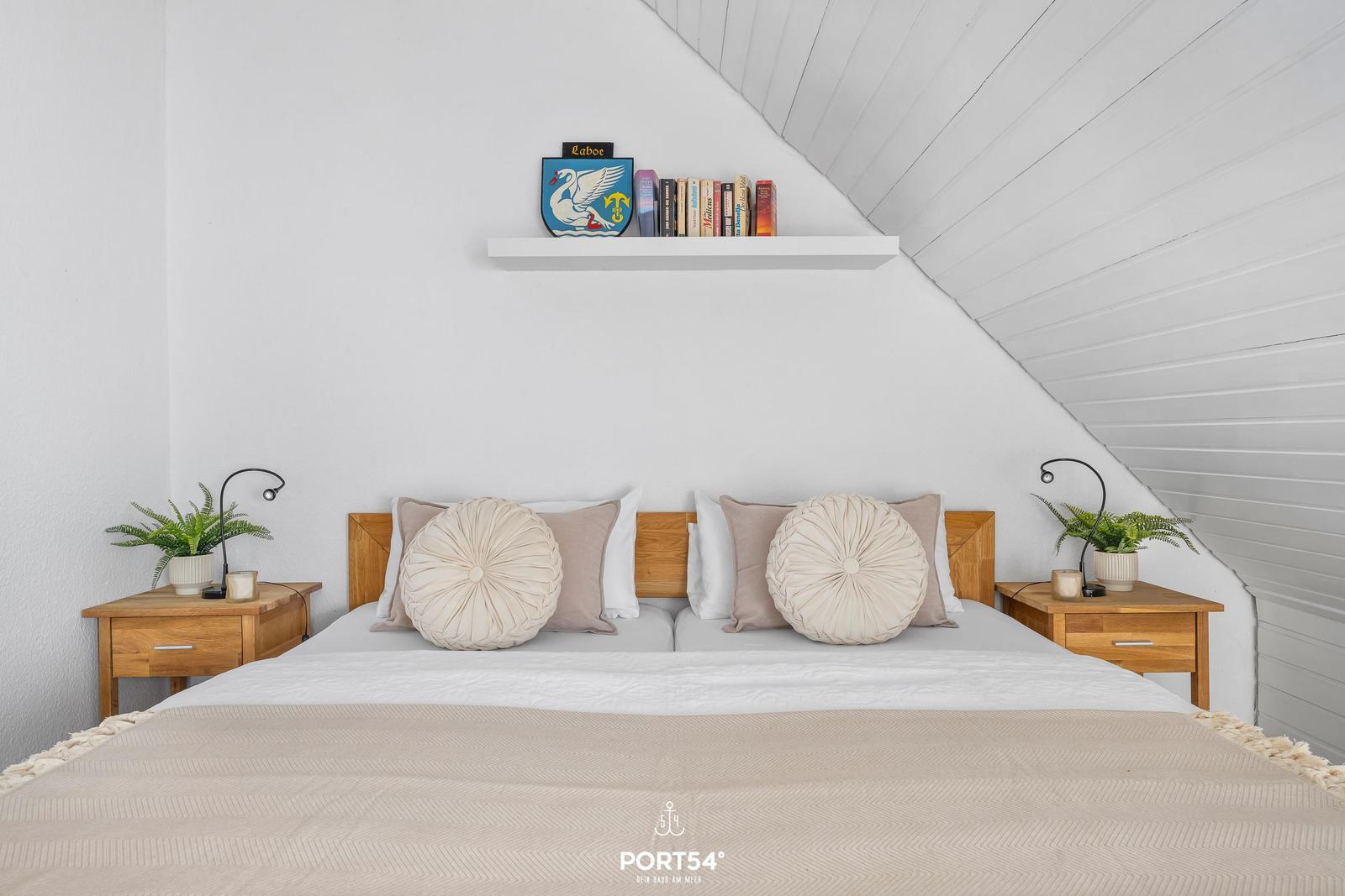 Schlafzimmer mit Dachschrägen, Bett, Nachttischen und Regal mit Büchern.