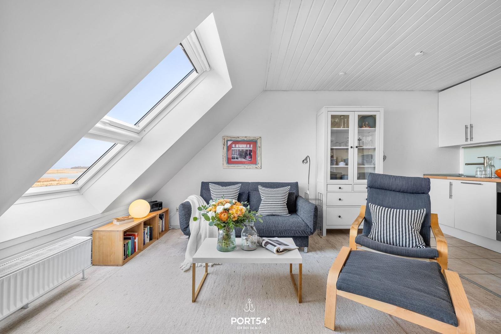 Wohnbereich mit Sofa, Sessel und Blick durch Dachfenster